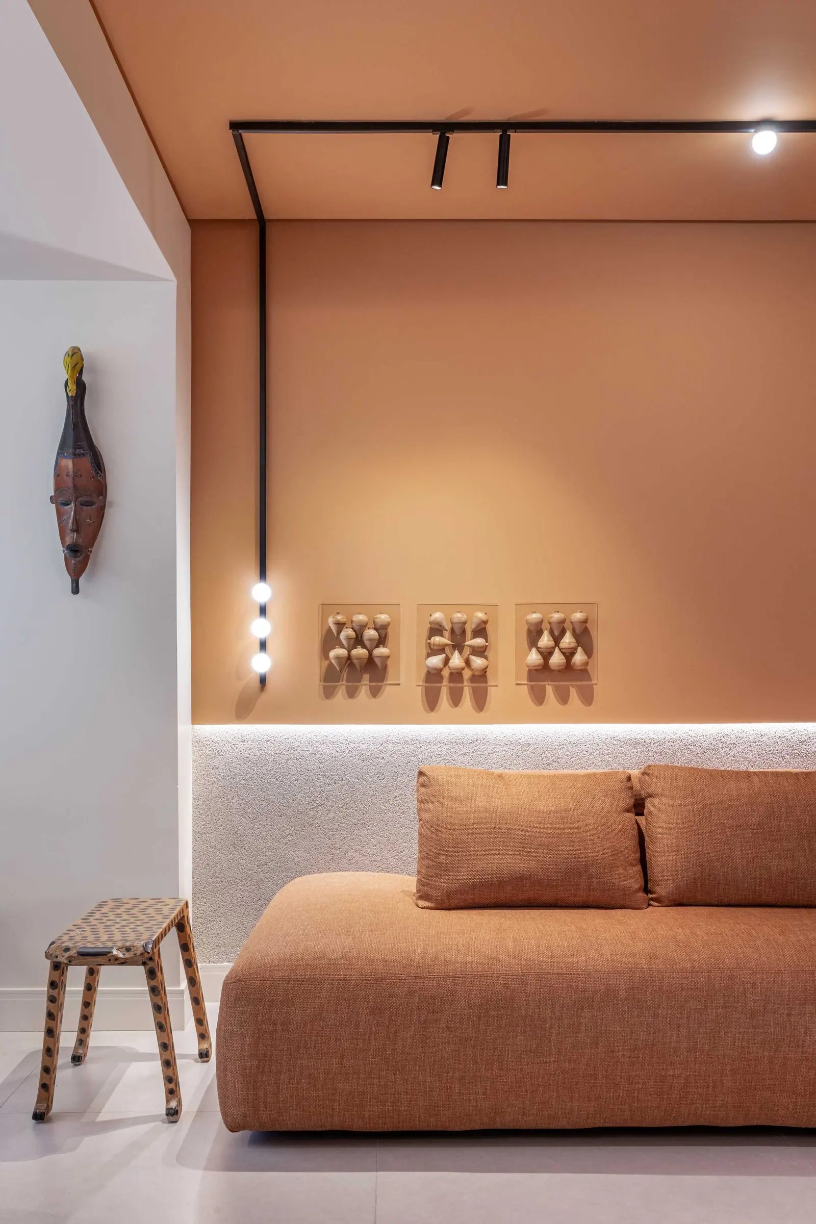 Sofá terracota sob trilho de luz e peças decorativas na parede