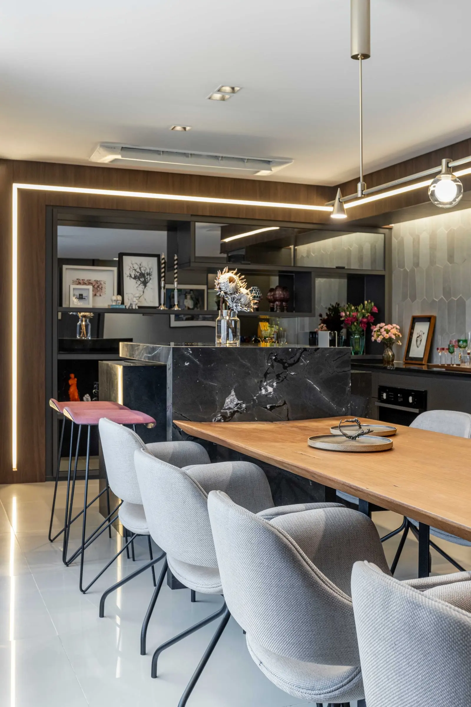 Mesa de jantar em madeira com cadeiras cinza e cozinha aberta ao fundo