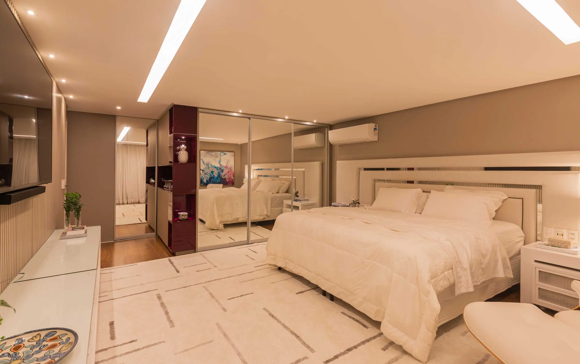 Suíte com cama branca, tapete geométrico e armários espelhados